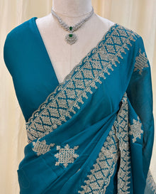 Teal blue georgette saree with golden white embroidery.