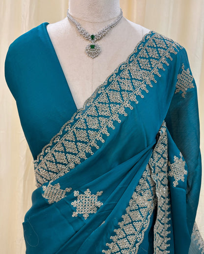 Teal blue georgette saree with golden white embroidery.