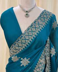 Teal blue georgette saree with golden white embroidery.