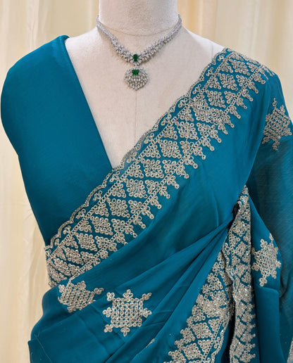 Teal blue georgette saree with golden white embroidery.